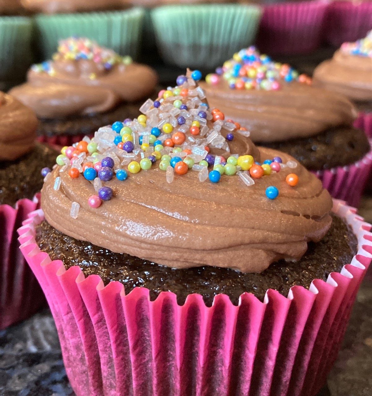 A tray of freshly frosted vanilla cupcakes with pastel sprinkles from the Crafty Café.