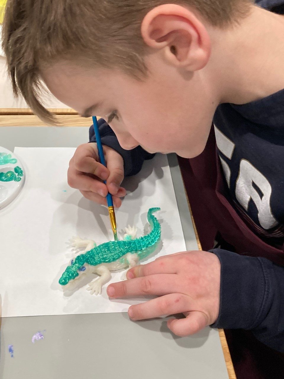 A child painting a small alligator figurine.