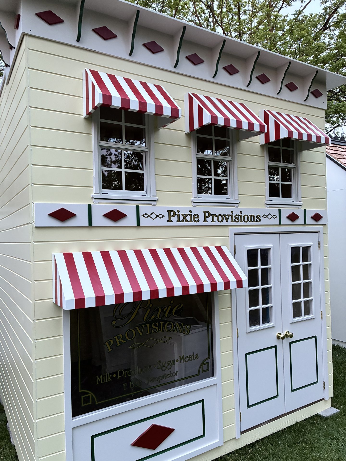 Pixie Provisions playhouse exterior — cream with red and white awnings.